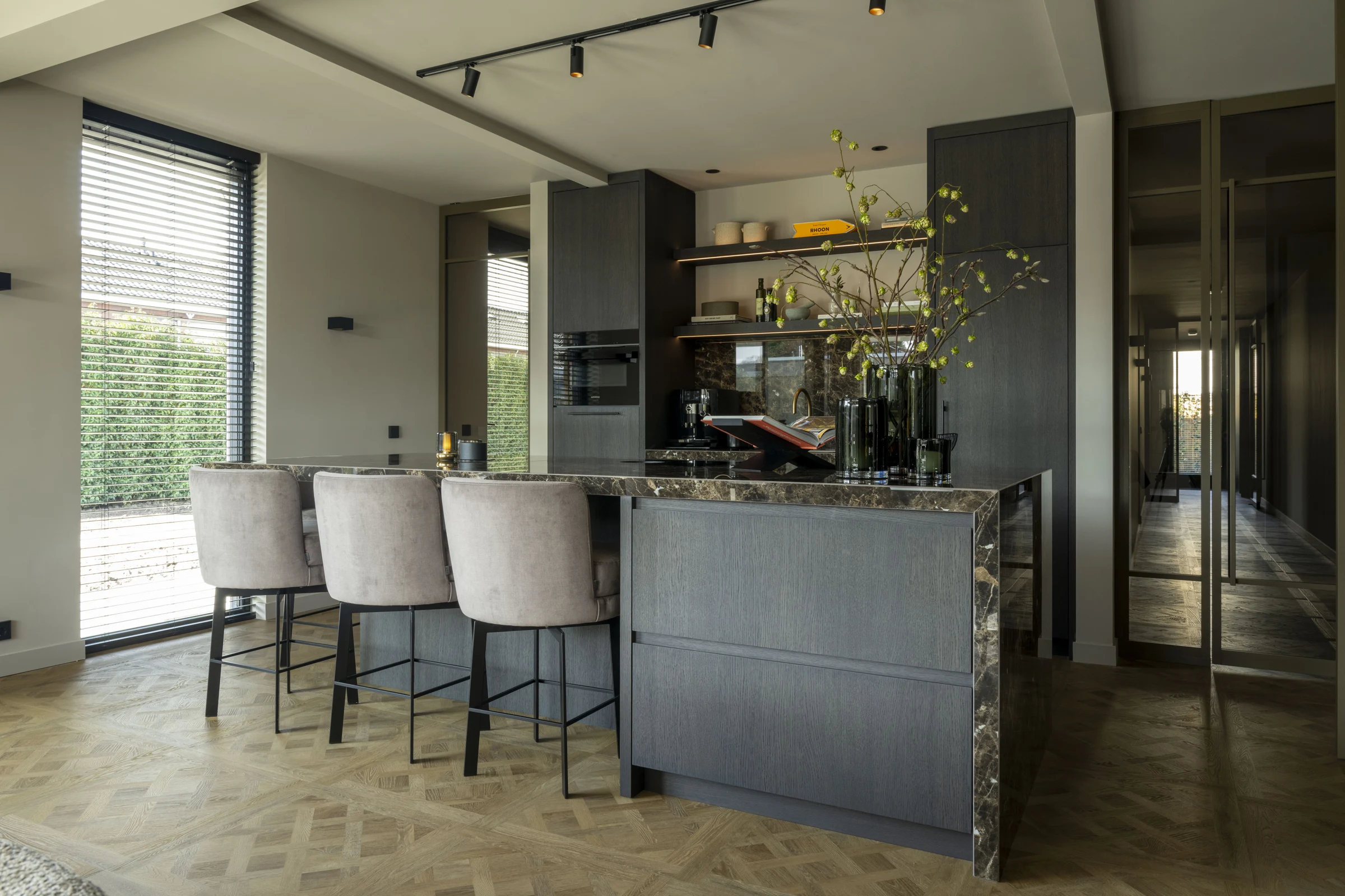 Luxe keuken met donker maatwerk, natuursteen en zachte gestoffeerde barkrukken
